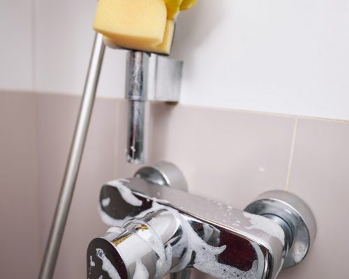 Cropped photo of cleaner wiping stainless steel wall-mounted shower holder with damp sponge